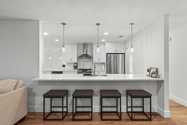 kitchen featuring appliances with stainless steel finishes, a sink, wall chimney range hood, and a breakfast bar area