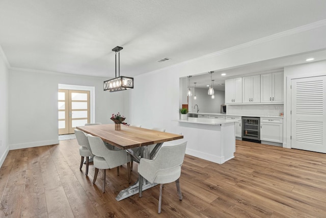 dining area with ornamental molding, beverage cooler, visible vents, and wood finished floors