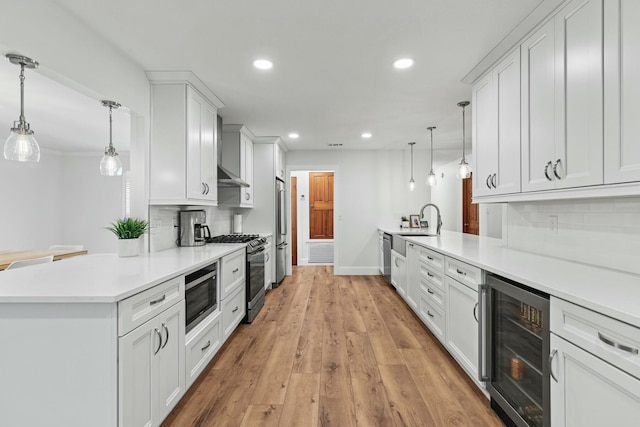 kitchen with beverage cooler, a peninsula, appliances with stainless steel finishes, and light wood finished floors