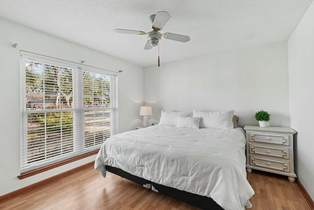 bedroom with a textured ceiling, ceiling fan, wood finished floors, and baseboards