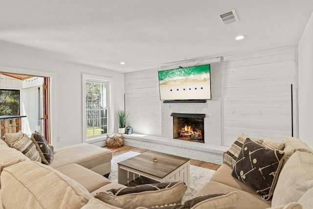 living room with wooden walls, visible vents, wood finished floors, a fireplace, and recessed lighting