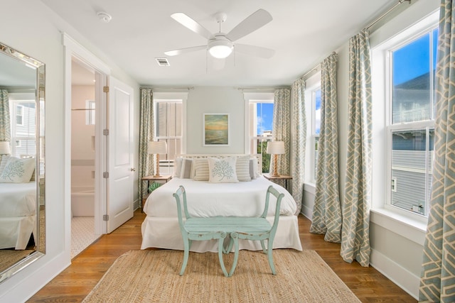 bedroom featuring ceiling fan, ensuite bathroom, wood finished floors, visible vents, and baseboards