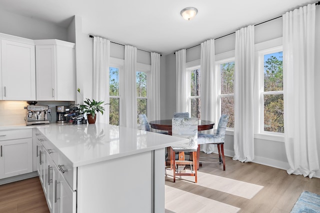 kitchen with white cabinets, a peninsula, light countertops, light wood-style floors, and backsplash