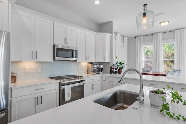 kitchen featuring light countertops, backsplash, appliances with stainless steel finishes, white cabinetry, and a sink