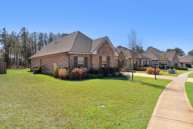 view of front of home with a shingled roof, a front lawn, and brick siding