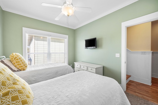 bedroom with a wainscoted wall, wood finished floors, a ceiling fan, and crown molding