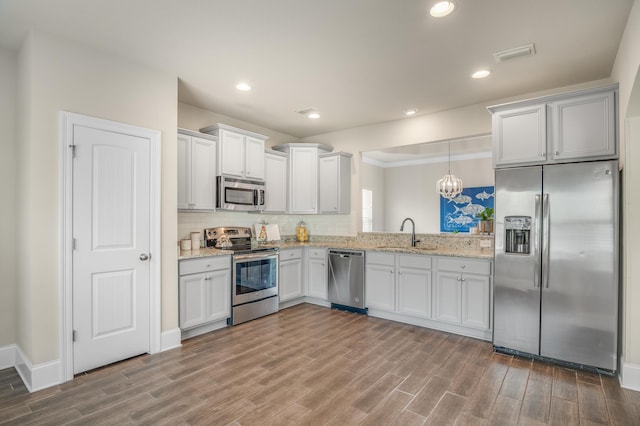 kitchen featuring wood finished floors, hanging light fixtures, appliances with stainless steel finishes, and a sink