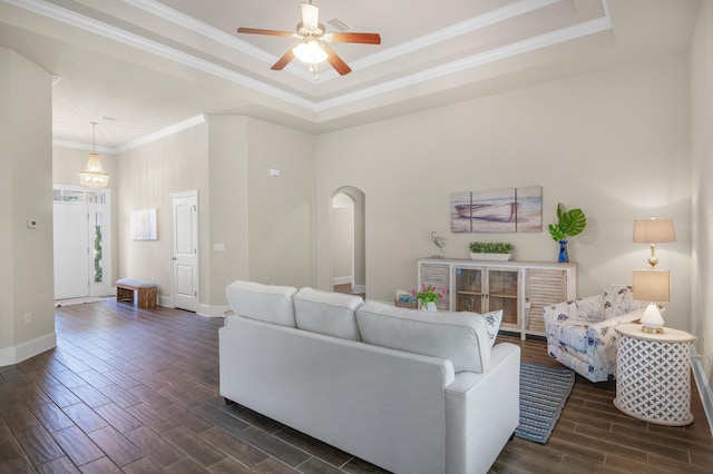 living room featuring wood finish floors, arched walkways, a tray ceiling, ornamental molding, and baseboards