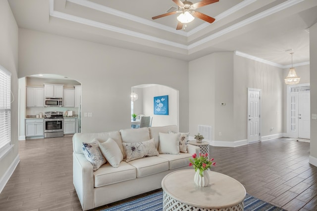 living area with arched walkways, a tray ceiling, dark wood-type flooring, and crown molding