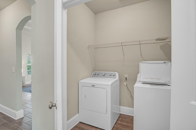 laundry area featuring laundry area, baseboards, arched walkways, washer and clothes dryer, and wood finish floors