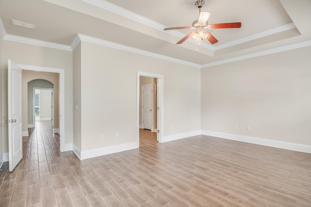 empty room with light wood-type flooring, visible vents, a tray ceiling, and arched walkways