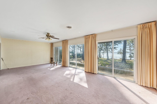 carpeted empty room with ceiling fan and brick wall