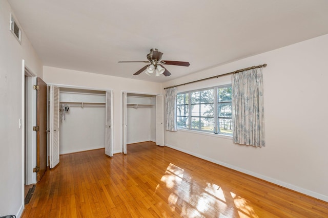 unfurnished bedroom featuring multiple closets, ceiling fan, and wood-type flooring