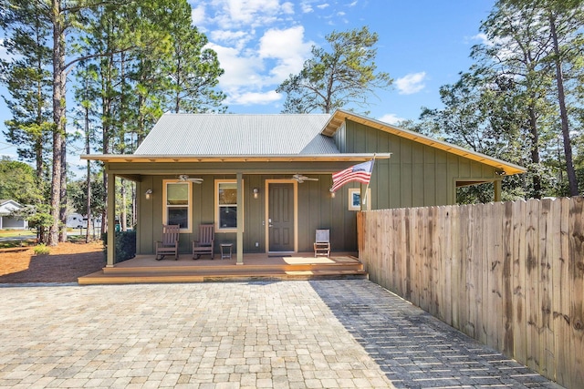 view of front facade with metal roof, covered porch, fence, a ceiling fan, and board and batten siding