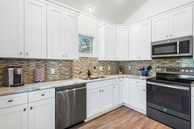 kitchen featuring lofted ceiling, backsplash, appliances with stainless steel finishes, white cabinetry, and a sink