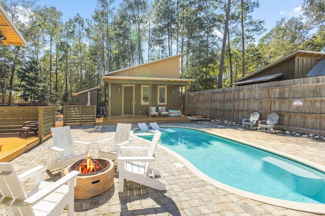 view of pool with an outbuilding, an exterior structure, fence, a fire pit, and a wooden deck