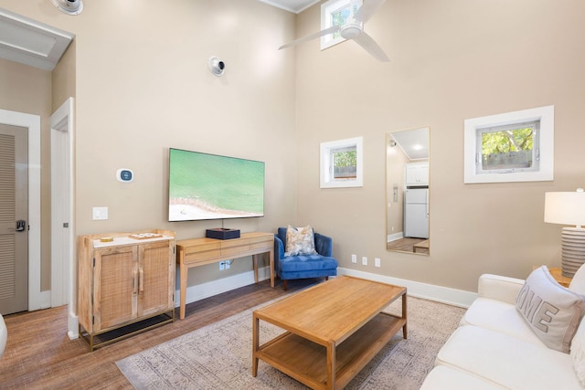 living room with a ceiling fan, a high ceiling, baseboards, and wood finished floors