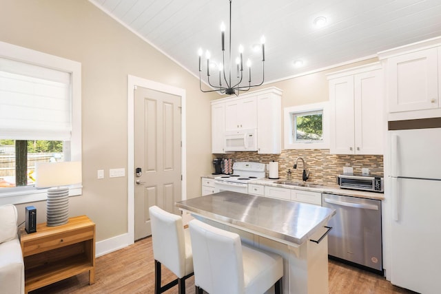 kitchen with white appliances, a center island, white cabinetry, pendant lighting, and a sink