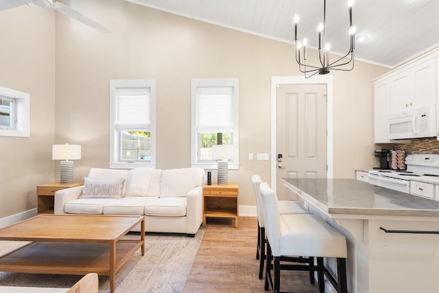 kitchen featuring white appliances, lofted ceiling, decorative light fixtures, a kitchen bar, and white cabinetry