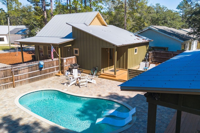 rear view of house with board and batten siding, fence, a fenced in pool, and a patio