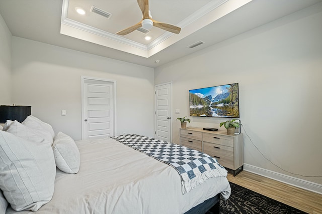 bedroom with a tray ceiling, ceiling fan, crown molding, and hardwood / wood-style flooring