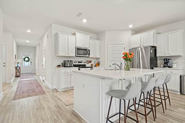 kitchen featuring white cabinetry, a center island with sink, stainless steel appliances, and a kitchen breakfast bar