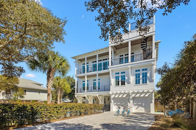 raised beach house featuring a balcony, decorative driveway, fence, and a garage