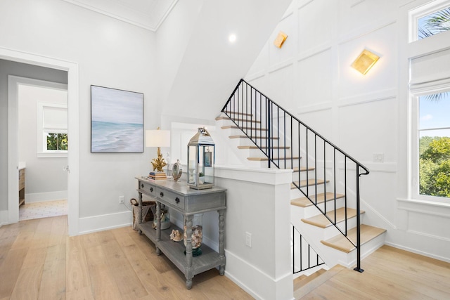 stairway featuring a decorative wall, crown molding, baseboards, and wood finished floors