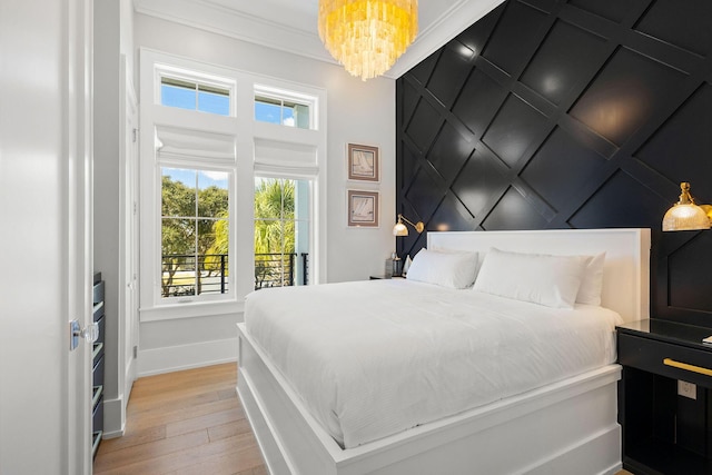 bedroom featuring light wood-style flooring, crown molding, a decorative wall, baseboards, and a chandelier