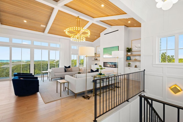 living room featuring a decorative wall, wood ceiling, a glass covered fireplace, light wood-style floors, and a notable chandelier