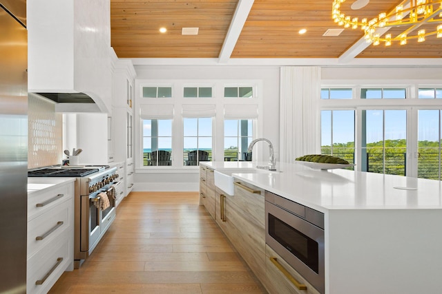 kitchen featuring beam ceiling, light wood-style flooring, custom range hood, a sink, and high end appliances