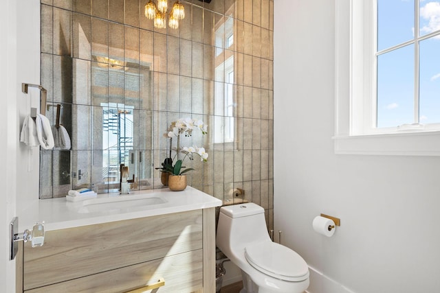 bathroom with tile walls, a notable chandelier, toilet, and vanity