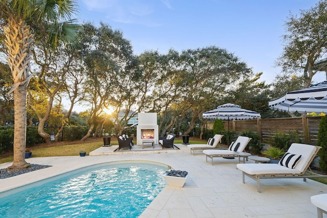 view of swimming pool with a patio, fence, a fenced in pool, and a lit fireplace