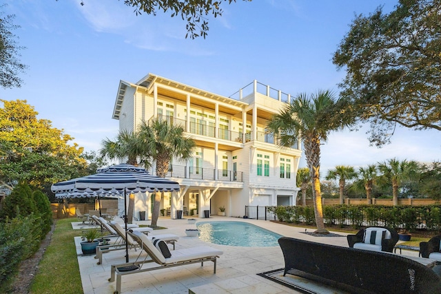 rear view of property with a balcony, fence, a patio area, and an outdoor pool