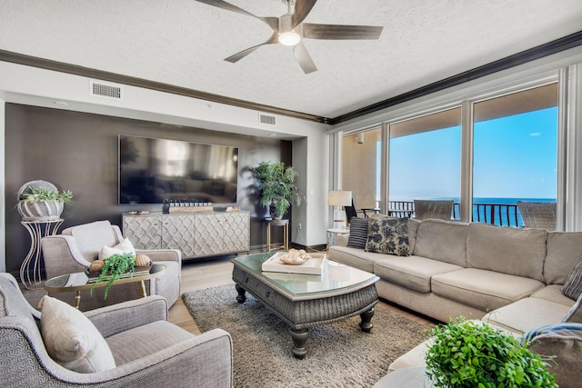 living area with visible vents, ornamental molding, a textured ceiling, and wood finished floors