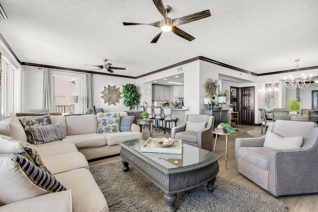 living area featuring ornamental molding, a textured ceiling, light wood finished floors, and ceiling fan with notable chandelier