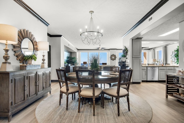 dining room with light wood-style flooring, a textured ceiling, ornamental molding, and a notable chandelier