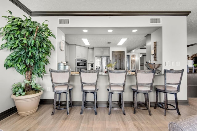 kitchen with a textured ceiling, a peninsula, visible vents, light wood-type flooring, and stainless steel fridge with ice dispenser