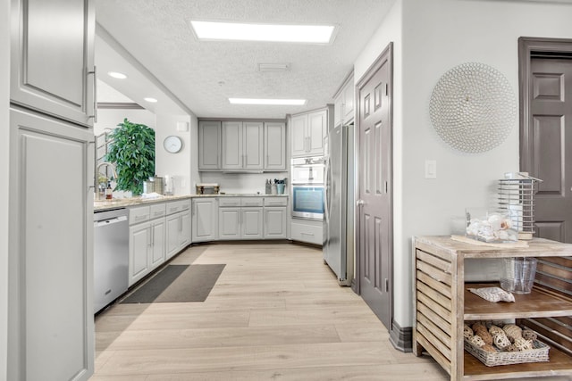 kitchen with appliances with stainless steel finishes, gray cabinetry, light wood-style flooring, and a textured ceiling