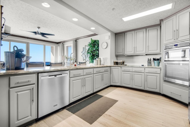 kitchen with appliances with stainless steel finishes, light wood-type flooring, gray cabinetry, and a ceiling fan