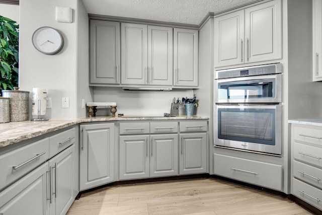 kitchen featuring light wood-style flooring, black electric cooktop, a textured ceiling, gray cabinets, and stainless steel double oven