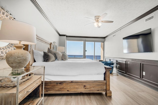 bedroom featuring visible vents, a wainscoted wall, light wood-style flooring, a textured ceiling, and crown molding