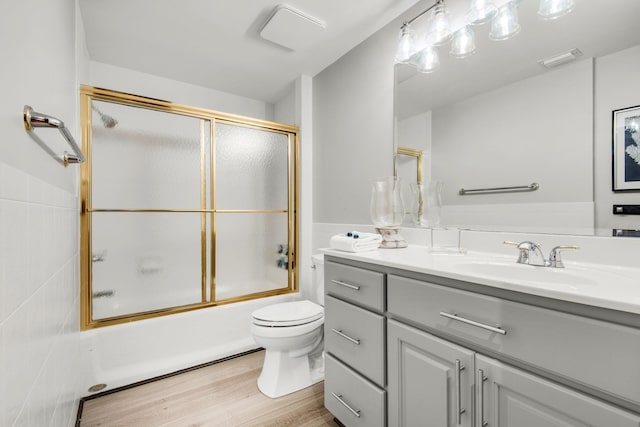 bathroom featuring visible vents, toilet, combined bath / shower with glass door, vanity, and wood finished floors