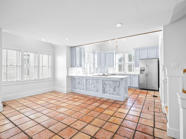 kitchen featuring lofted ceiling, light countertops, a sink, a peninsula, and stainless steel fridge with ice dispenser