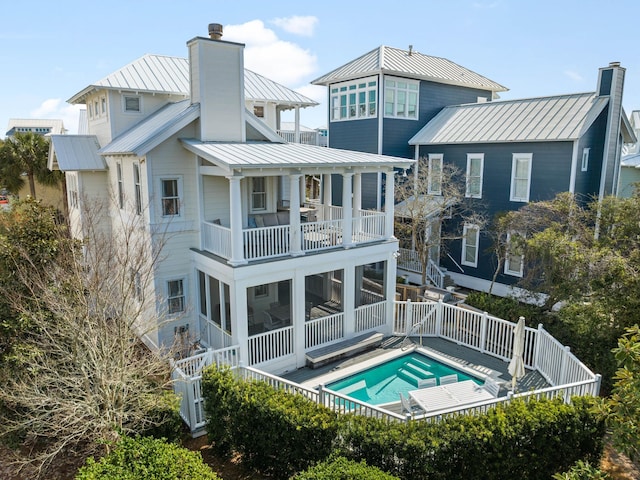 rear view of property with metal roof, a standing seam roof, a chimney, and a balcony