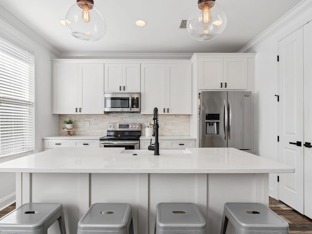 kitchen with stainless steel appliances, an island with sink, white cabinetry, and decorative backsplash