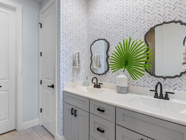 full bathroom with double vanity, a sink, baseboards, and wallpapered walls