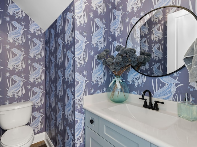 half bath featuring baseboards, vanity, toilet, and wallpapered walls