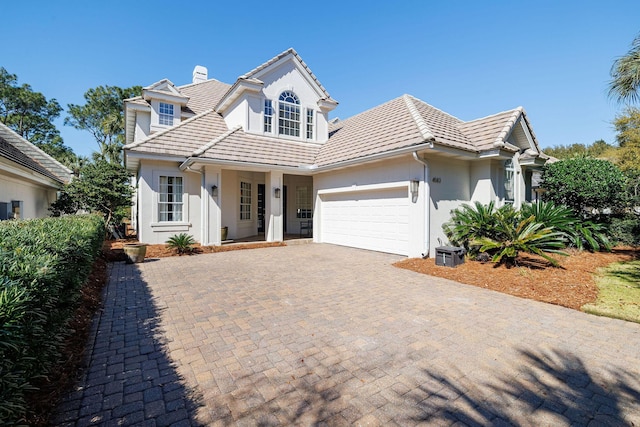 view of front of property featuring a garage, decorative driveway, a chimney, and stucco siding