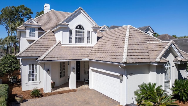 view of front of house with a tiled roof, stucco siding, a chimney, decorative driveway, and a garage